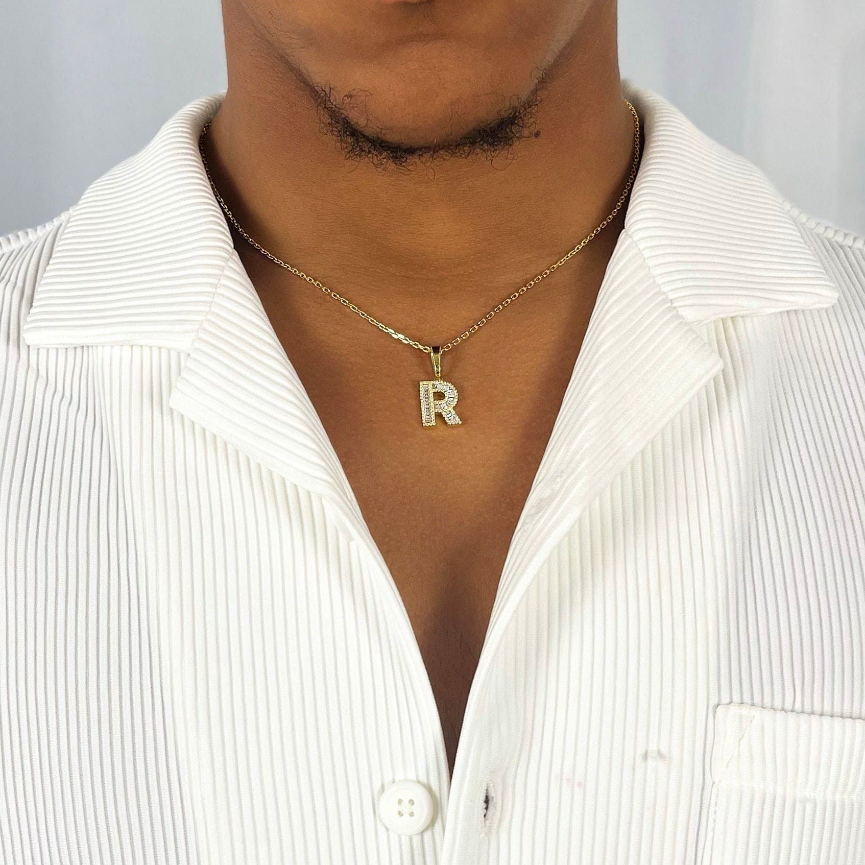 This is a mid shot of a model showcasing our 9k yellow gold baguette moissanite letter pendant R necklace around his neck